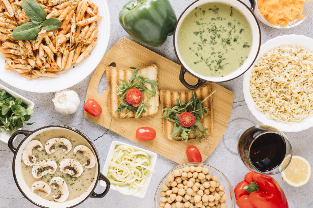 tavola imbandita di alimenti di vario tipo: zuppa, pasta, toast, ceci, vino, peperoni.